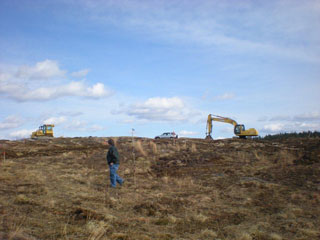 Brad surveying a field of dirt with construction machines further away