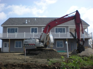 Septic field covered in dirt and no longer visiable, siding finished, cold storage has a door, and there is a backhoe front and center
