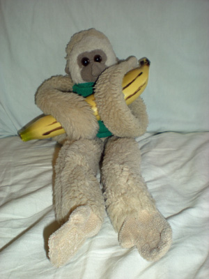 A gibbon monkey plushie wearing a green shirt, clutching a banana